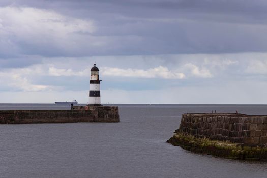 Famous Seaham harbour lighthouse with black and white stripes stands at the end of a stone wall, against a backdrop of moody storm clouds and brick foreground. Durham Heritage Coast, UK. Canon EOS 90D