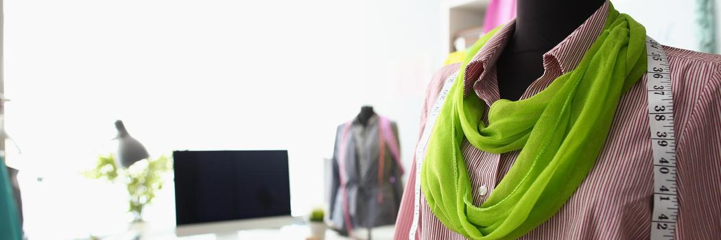 Close-up of mannequin with unique combination of red shirt and green scarf. Creative workspace in cozy small studio. Small family business, atelier concept
