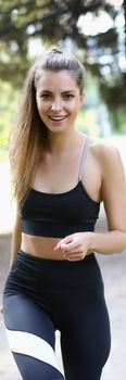 Portrait of smiling pretty young woman running marathon in sportswear. Race track competition in nature, amateur participant. Runner, sport, hobby concept