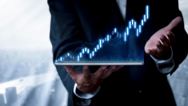 Hand of businessman holding tablet analysis stock market graph growth and increase of chart positive indicators. Hand holding tablet show stock chart on light gray background. copy space banner