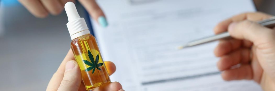 Close-up of hemp extract oil in bottle with leaf sign on it. Doctor fill patient information in prescription. Alternative medicine, healthcare, cbd concept