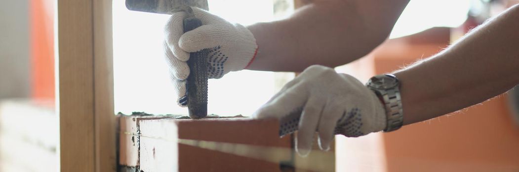 Close-up of foreman use special tool working with brick building wall in room. Progress on construction site, man busy at work. Renovation, builder concept