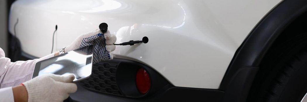 Close-up of male automechanic hands holding modern digital tablet and car tube in white gloves. Smart mechanic at service station. Automotive check concept