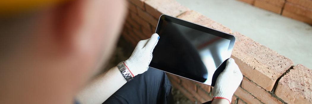 Close-up of construction worker holding tablet with black turned off screen. Pause during working day, kill time with device. Renovation, mockup concept