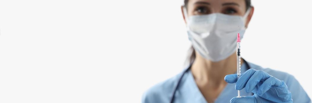 Close-up of female nurse holding syringe with vaccine liquid wear face mask. Doctor and cure vaccine from dangerous virus. Medicine, healthcare concept