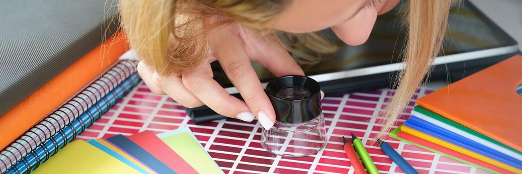 Close-up of designer woman searching for perfect shadow of red using magnifying glass. Work on big project for flat interior. Art, design agency concept