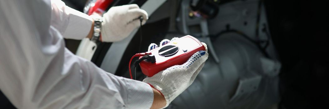 Close-up of mechanics hand using multimeter to measure voltage of car battery. Worker does inspection of auto. Repair service and car insurance concept