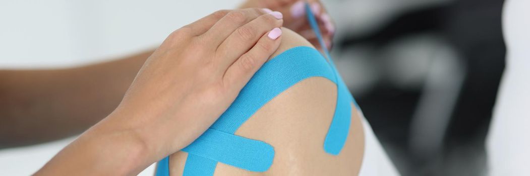 Close-up of physiotherapist apply kinesiology tape to patient knee in clinic. Rehabilitation after injury or accident. Physical therapy, healthcare concept