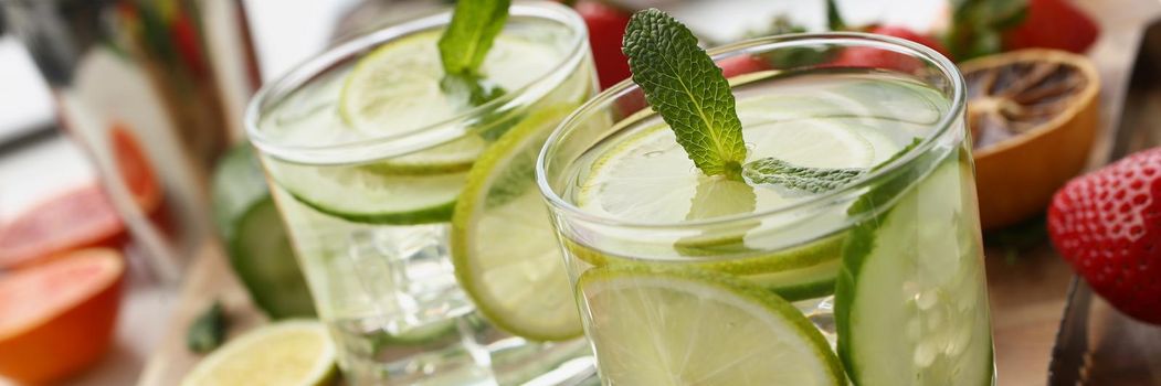 Close-up of pair of tasty refreshing cocktails with lemon and cucumber slices decorated with mint. Prepare for home party, homemade drinks. Punch concept