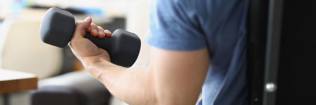 Close-up of strong man lifting dumbbell to achieve personal sport goal. Training at home, good morning habit for health. Sport, weight loss, health concept