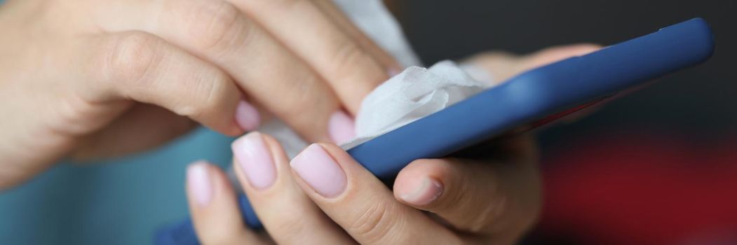 Close-up of woman cleaning mobile phone screen with wet wipe from bacteria. Take care of smartphone condition, prevent infection spread. Technology concept