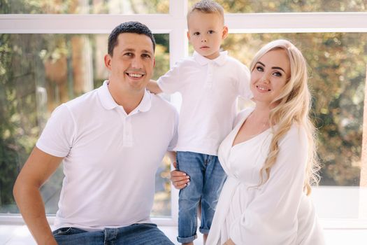 Happy photosession of pregnant woman her husband and their son. Family waiting for baby. White closes family look concept.