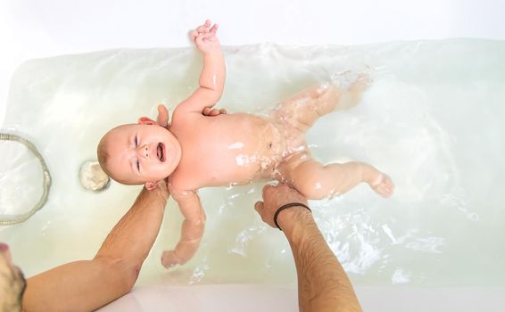 Little baby crying is afraid to swim in the bathroom. Selective focus. People.
