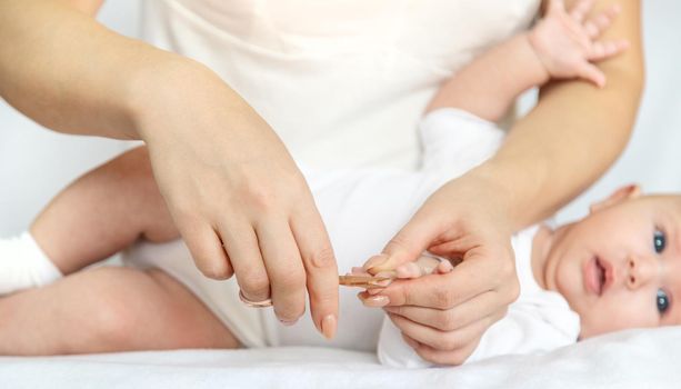 Mother cuts baby's fingernails on light background. Selective focus. people.