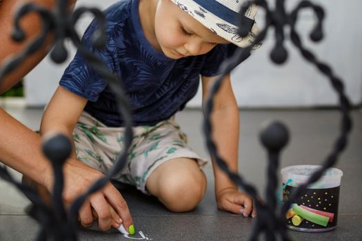 Little boy and his mother drawing with colorful chalk crayons on concrete sidewalk top view. The mother helps to concentrate with the help of her hand, she teaches her child