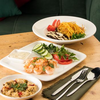 A dinner table with meals with hummus, shrimp, vegetables and beef