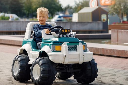 The happy blond boy is very focused, driving a big green toy SUV.