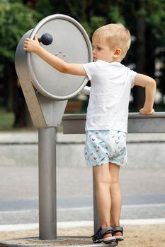 A little boy wearing shorts and a t-shirt plays with a tap in a public park.