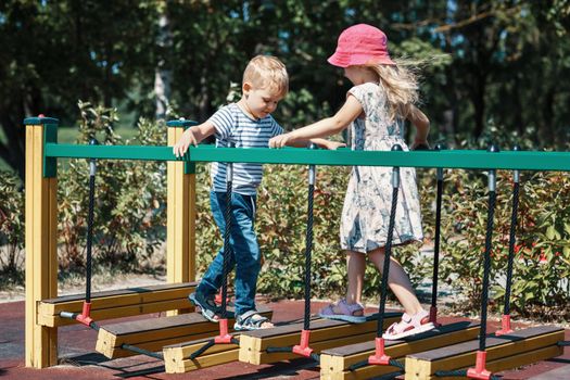 The boy and girl meet each other on a monkey bridge at a city children's playground.