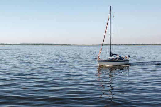 A quiet summer day and a lonely yacht with lowered sails and the German flag in the lagoon