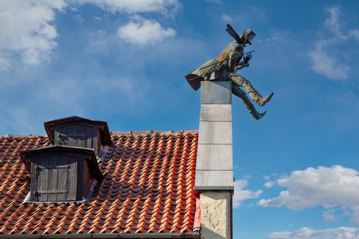 The chimney sweep on roof of house of Klaipeda in Lithuania. Red tiled roof and blue sky with white clouds in the background.