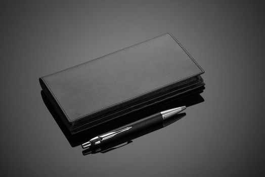 A closeup of fashionable leather men's wallet and pen on a black background