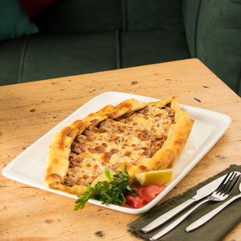 A traditional Turkish baked pide in a white plate on a wooden table