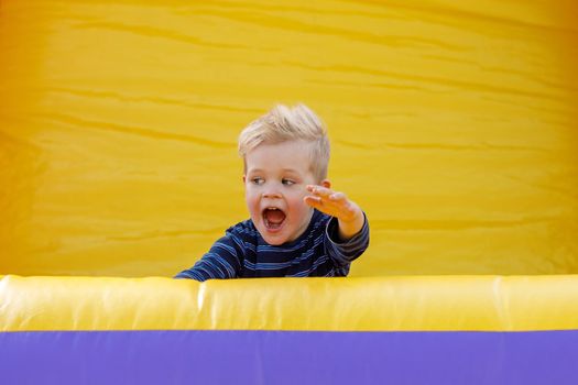 A child is happy and shouts on an inflatable yellow playground. Amusement park for children. Inflatable trampoline for jumping and fun. Rest in the summer in the fresh air.