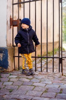 Little careful boy in in the old town. Lovely kid looking back to make sure no one sees him, he tries to get through the gate into the yard. Outdoor walks in fall.