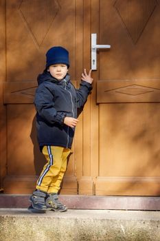 Little boy knocking the brown door in the down city.