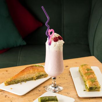 A healthy strawberry smoothie in a mug with drinking tubules next to baklavas on a wooden table