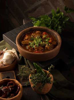 A close up shot of a meat stew and herbs in the background