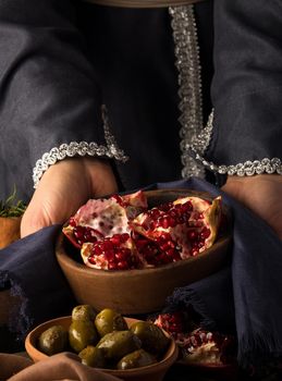 A vertical photo of woman's hands holding a bowl of pomegranate