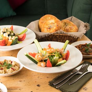 A dining table full of delicious salad on a white plate next to basket of bread