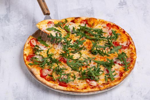 An angle shot of a spatula taking one piece of an arugula pizza.