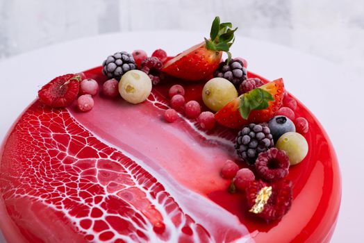 An angle shot of a mirror glaze cake decorated with berries.