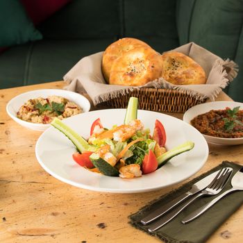 A dining table full of delicious salad on a white plate next to basket of bread