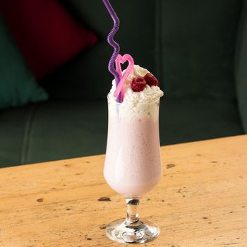 A closeup shot of a healthy strawberry smoothie in a mug with drinking tubules on a wooden table