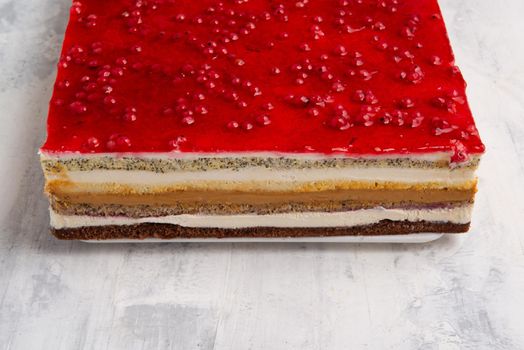 An angle shot of a multi-layered cake with a red currant jelly layer on top.