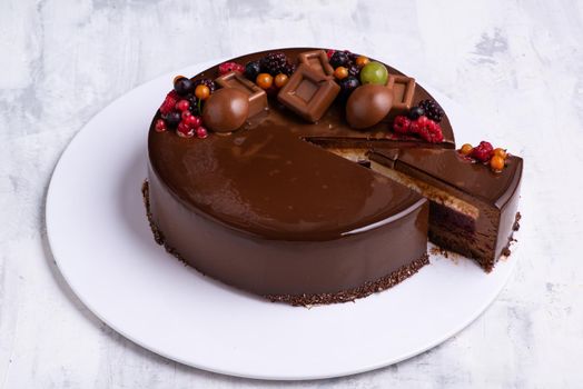 An angle shot of a chocolate glaze cake with one piece cut out decorated with berries.