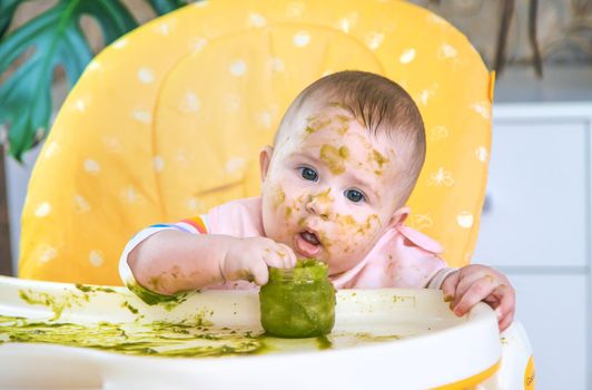 Little baby eats broccoli puree himself. Selective focus. People.