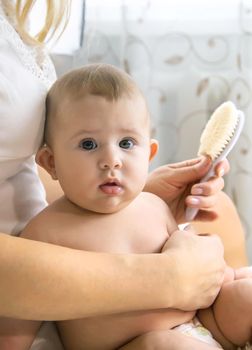 The mother is combing the little baby's hair. Selective focus. People.