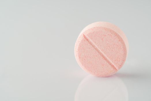 A close-up shot of a pink vitamin pill on a white reflecting surface.