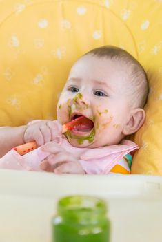 Little baby is eating broccoli vegetable puree. Selective focus. People.