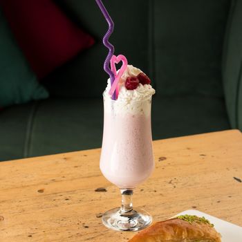 A healthy strawberry smoothie in a mug with drinking tubules next to baklava on a wooden table