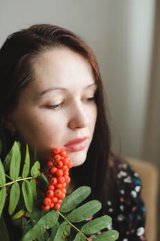 Portrait of a beautiful young brunette woman with red lipstick and rowan berries.