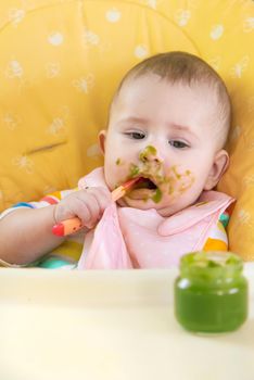 Little baby is eating broccoli vegetable puree. Selective focus. People.