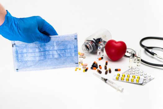 A closeup of a person's hand with gloves holding medical masks and medicines on a table