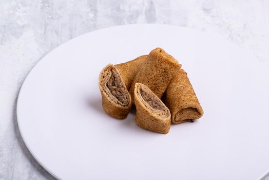 A plate of stuffed pancakes with meat on a white table