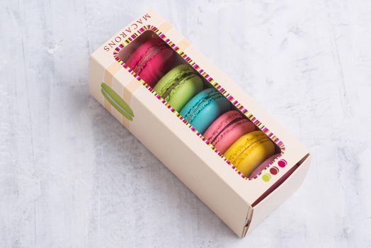 An angle shot of colorful French macarons placed in a cute box with a transparent top.